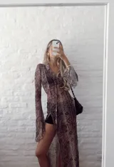 Vestido largo de gasa transparente con estampado de piel de serpiente en tonos marrones. Tiene cuello camisero, mangas largas acampanadas y abertura frontal con cordones.