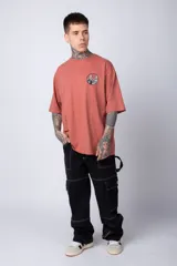 Remera color ladrillo de corte oversize, con cuello redondo y mangas cortas. Estampado pequeño en el pecho con un diseño circular en blanco y negro.