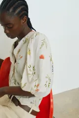 Blusa de lino color blanco con estampado de flores, cuello redondo, cierre de botones y mangas globo tres cuartos con puños elásticos.