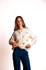 Saco de punto color rojo, con cuello polo y cierre frontal de botones blancos. Presenta flores bordadas en relieve de diferentes colores (azul, amarillo, verde, naranja, rosado) y mangas largas con diseño de burbujas.