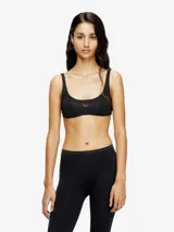 Sujetador deportivo negro, corte crop top, con banda elástica ancha bajo el busto que lleva un logo metálico en el centro.