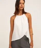 Blusa blanca sin mangas, con cuello halter y diseño cruzado en el frente.