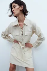 Vestido de manga larga color beige, con ojalillos en el frente y bolsillos.