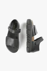 Sandalia plana negra de cuero, con tiras anchas cruzadas y ajuste con velcro.