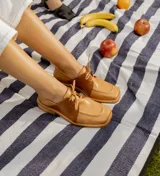 Zapato acordonado de cuero vacuno color marrón oscuro, con suela de goma, horma cuadrada y tacón bajo.