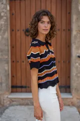 Chomba tejida de punto con cuello estilo polo y escote en V. De manga corta y calce relajado, cuenta con diseño de ondas horizontales en colores combinados: negro, naranja, blanco y lila.