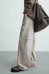 Pantalón de algodón color beige claro, estilo relaxed fit, con cintura ajustable mediante cinturón de tela a juego. Presenta cinco bolsillos, bolsillos laterales de vivo y costuras laterales giradas hacia adelante.