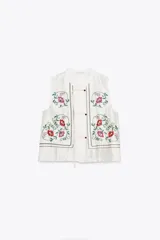 Top blanco de cuello mao y sin mangas, con bordados florales en el frente y cierre con botones.