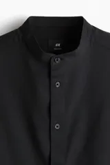 Camisa negra de corte estándar, con cuello mao, tapeta clásica y mangas largas con puños abotonados.