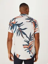 Camisa blanca de manga corta con estampado de hojas en negro y gris, cuello clásico y corte recto.