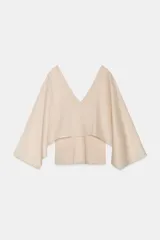 Top de punto color beige con escote en V tanto en el delantero como en la espalda. Presenta mangas largas anchas de estilo kimono confeccionadas en un tejido fluido combinado.