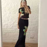 Conjunto de top y falda larga de color negro con estampado de flores rojas y verdes. El top es de mangas cortas y la falda tiene elástico en la cintura.