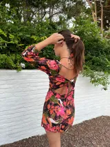 Vestido corto con estampado floral en tonos rosa y lila, escote cuadrado con detalle fruncido y abertura en el centro, mangas largas abullonadas y falda con tajo lateral.