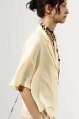Camisa color amarillo pálido de tejido fluido, con cuello solapa, escote pico, manga corta, bolsillo de parche en el pecho y cierre frontal con botones.