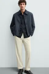 Pantalón chino color beige, corte recto, con bolsillos laterales y traseros. Cierre frontal con cremallera y botón.