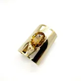 Brazalete dorado ancho de metal brillante con una piedra de cristal topacio ovalada engarzada en el centro. Es ajustable.