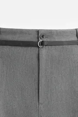 Pantalón gris de corte ancho con pliegues frontales y cinturón fino negro.