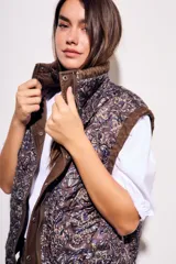 Chaleco reversible de algodón con acabado lavado y diseño acolchado con pespuntes ondulados. Presenta cuello alto con cordón ajustable, cierre frontal de cremallera y botones a presión, bolsillos delanteros tipo parche y cordón de ajuste en el bajo.