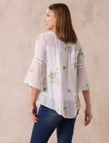 Blusa blanca de gasa con bordados florales, corte holgado, mangas 3/4 acampanadas con detalle de puntilla y forro interno.