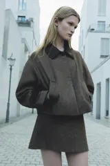Chaqueta corta de tweed gris con cuello solapa y puños de cuero negro. Cierre frontal con botones ocultos.