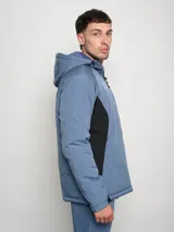 Campera corta de abrigo Umbro Crafted Pro, color negro con paneles laterales en gris. Presenta capucha con cordón ajustable, cierre frontal completo y logo de la marca bordado en el pecho.