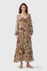 Vestido largo de gasa color beige con estampado floral en tonos rojos y verdes, escote en V con lazo y mangas largas abullonadas.