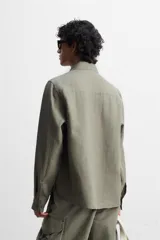 Sobrecamisa verde militar de lino, corte relaxed fit, con cuello solapa, manga larga con puños abotonados, bolsillos de parche con solapa en el pecho, aberturas laterales en el bajo y cierre frontal abotonado.