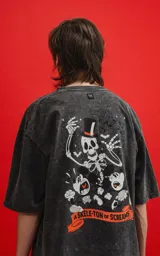 Remera oversize de algodón premium, color gris oscuro con efecto nevado (acid wash), con estampa frontal de calaveras inspiradas en Disney y texto "CHILLED BY BONE".