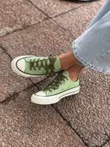 Zapatillas bajas de lona color blanco, con cordones marrones, puntera de goma y base blanca.