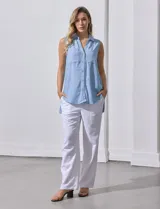 Camisa sin mangas color celeste, confeccionada en lino. Presenta cuello camisero, escote en V, abertura frontal con botones, dos bolsillos de parche en el pecho y terminación con botones en los laterales.