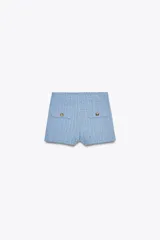 Shorts de tejido con textura color celeste, de tiro alto y cintura elástica. Presenta falsos bolsillos con solapa y botón metálico en el delantero.