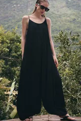 Mono de mujer color marrón oscuro, con escote redondo y tirantes finos. El tejido es satinado y plisado verticalmente. El pantalón es estilo bombacho con bajo abullonado ajustado con botón.