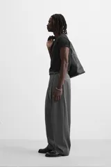 Pantalón gris de corte ancho con pliegues frontales y cinturón fino negro.