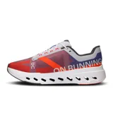 Championes de running On Cloudsurfer Next, color rojo y azul, con detalles en gris y blanco. Presentan tecnología CloudTec Phase para una amortiguación suave y reactiva.