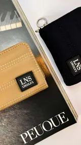 Billetera corta de tela capitoneada color negro, con cierre alrededor y tapa. Incluye varias reparticiones con tarjeteros y bolsillos internos. Correa de mano desmontable.