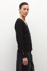 Cardigan negro de tejido fino, con escote en V y cierre frontal de botones plateados. Presenta aberturas en los puños.