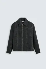 Sobrecamisa negra con textura de tejido bouclé y rayas verticales plateadas. Tiene cuello solapa, manga larga con puños abotonados, bolsillos laterales y cierre frontal con cremallera.