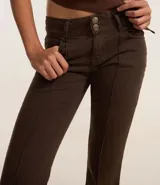 Pantalón flare de jeans color marrón con cintura doble, trabillas, abotonado doble, cierre tradicional, bolsillos y frisos delanteros.