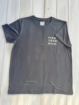 Remera negra de algodón y poliéster con cuello redondo y mangas cortas. Estampado en la espalda con dibujo lineal de montañas, cascada, árboles y camioneta con canoa en el techo.