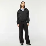 Cortavientos negro con capucha, cierre frontal con cremallera, mangas largas con puños elásticos y bolsillos laterales.