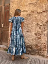 Vestido largo con estampado tie-dye en tonos azules y blancos, con mangas cortas con volados y falda con volados en el ruedo.