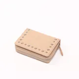 Billetera beige con cierre de cremallera y apliques de tachas metálicas.