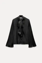 Blusa negra de cuello redondo con lazo en el mismo tejido. Manga larga acampanada y bajo recto.
