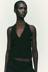Top negro con cuello halter, escote pico y espalda descubierta. Presenta detalle de frunces laterales y cierre frontal con botones.