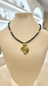 Collar corto con cuentas facetadas de color azul oscuro y dije irregular martillado de acero dorado.
