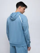 Canguro de felpa color crema con capucha, cordones y logo Umbro bordado en rojo. Presenta ribete rojo en hombros y bolsillo tipo canguro con cierre lateral.