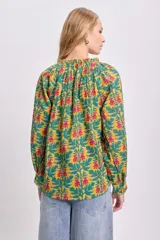 Blusa de manga larga con estampado floral en tonos mostaza, verde y rosa. Tiene cuello redondo con lazo ajustable.