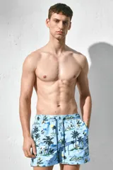 Short de baño celeste con estampado de palmeras, personas y paisajes playeros. Tiene elástico en la cintura y cordón de ajuste.
