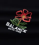 Remera de algodón negra, corte oversized, con estampa frontal de una flor estilizada en tonos rojo, amarillo y verde, y el texto "Balance ESTD. 1995" en blanco.