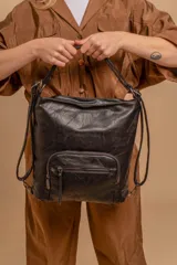 Cartera mochila color tostado, símil cuero, con compartimiento principal amplio y bolsillos frontales con cierre. Tiene correas ajustables para usar como mochila y asa superior para llevar al hombro.